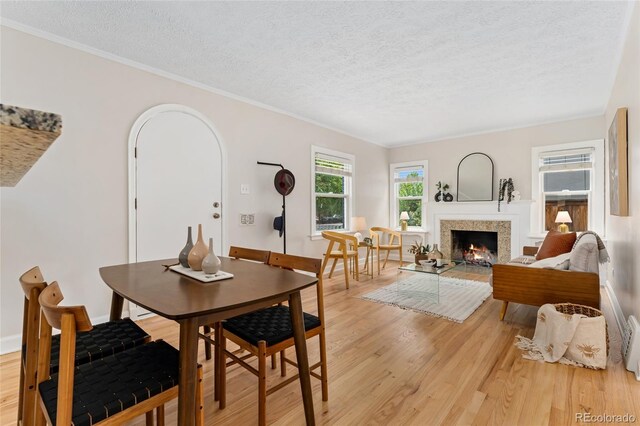 1691 Roslyn St, Denver, CO 80220 - dining area featuring light wood-style floors, a textured ceiling, a warm lit fireplace, baseboards, and ornamental molding