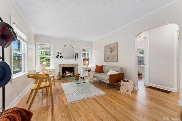 1691 Roslyn St, Denver, CO 80220 - living area featuring arched walkways, a textured ceiling, light wood finished floors, a fireplace with flush hearth, and baseboards
