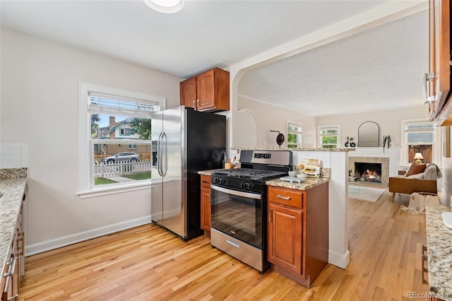 1691 Roslyn St, Denver, CO 80220 - kitchen featuring stainless steel appliances, brown cabinetry, light wood-type flooring, and open floor plan
