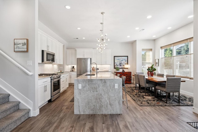 888 S Valentia St Unit 20-101, Denver, CO 80247 - kitchen with stainless steel appliances, tasteful backsplash, a center island with sink, wood finished floors, and recessed lighting