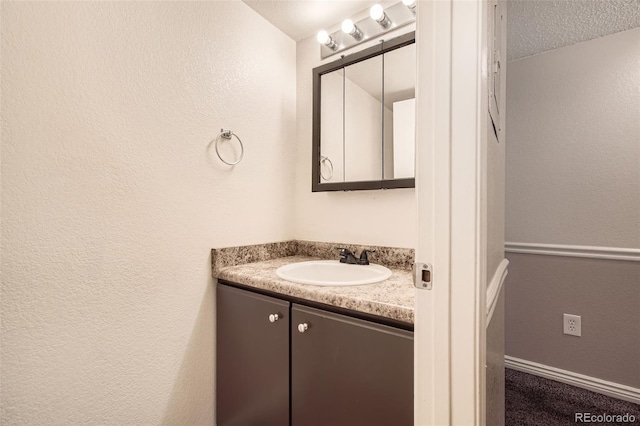 bathroom with vanity, a textured wall, baseboards, and a textured ceiling