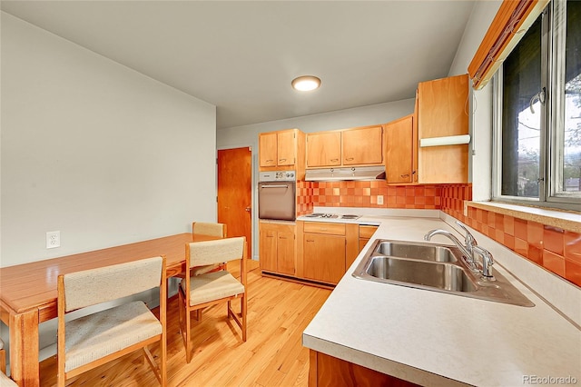 kitchen with wall oven, a sink, light countertops, under cabinet range hood, and light wood-style floors