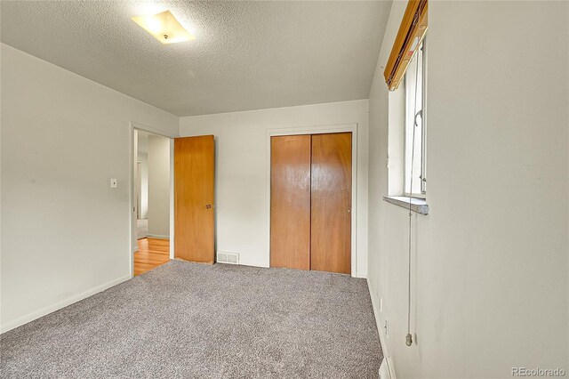 unfurnished bedroom featuring carpet floors, a closet, a textured ceiling, and baseboards