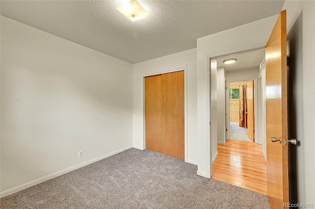 unfurnished bedroom with light carpet, baseboards, a closet, and a textured ceiling