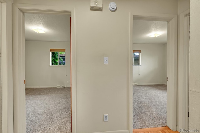 corridor featuring a textured ceiling, carpet flooring, and baseboards