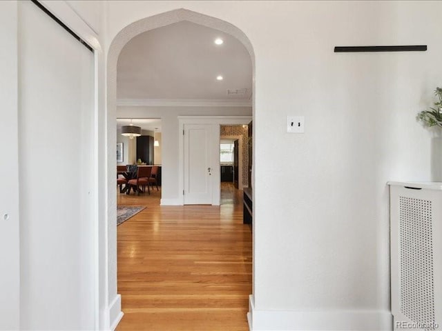 corridor with arched walkways, crown molding, and light wood finished floors