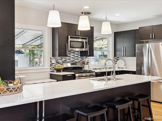 kitchen featuring appliances with stainless steel finishes, a sink, light countertops, a kitchen breakfast bar, and recessed lighting