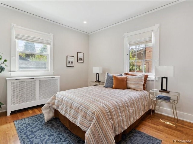 bedroom with radiator, ornamental molding, multiple windows, wood finished floors, and baseboards