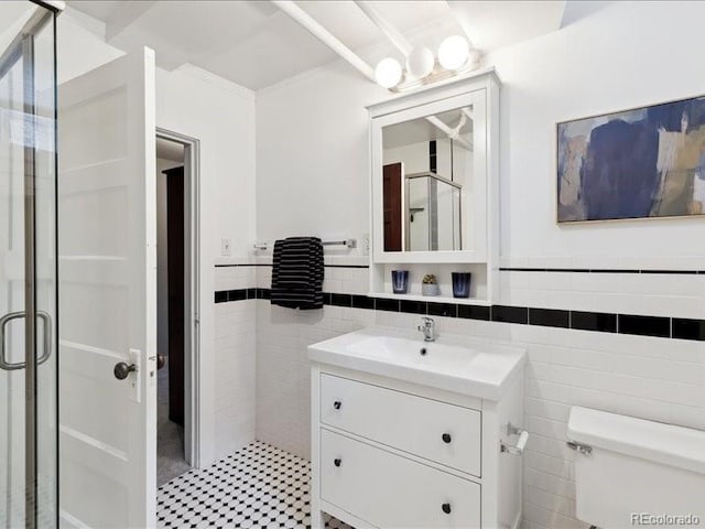 bathroom with tile walls, a shower stall, a wainscoted wall, toilet, and vanity