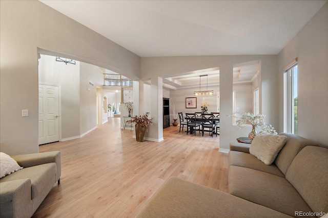 living room featuring light wood finished floors, a chandelier, baseboards, lofted ceiling, and arched walkways