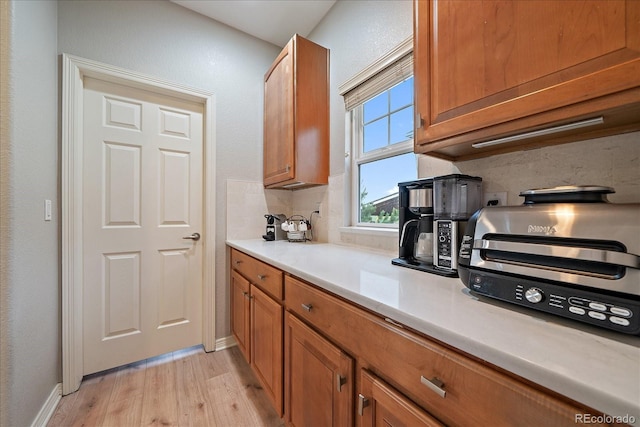kitchen featuring light wood-style flooring, brown cabinets, light countertops, and decorative backsplash