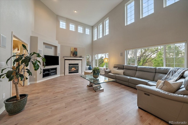 living area featuring a high ceiling, light wood-style flooring, a glass covered fireplace, and recessed lighting