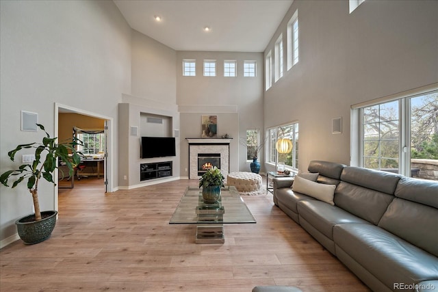 living area featuring a high ceiling, light wood-style floors, baseboards, a glass covered fireplace, and recessed lighting