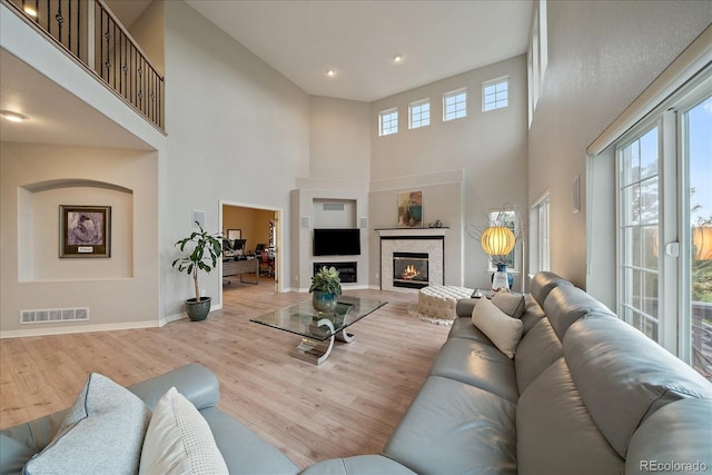 living room featuring a towering ceiling, wood finished floors, baseboards, recessed lighting, and a glass covered fireplace