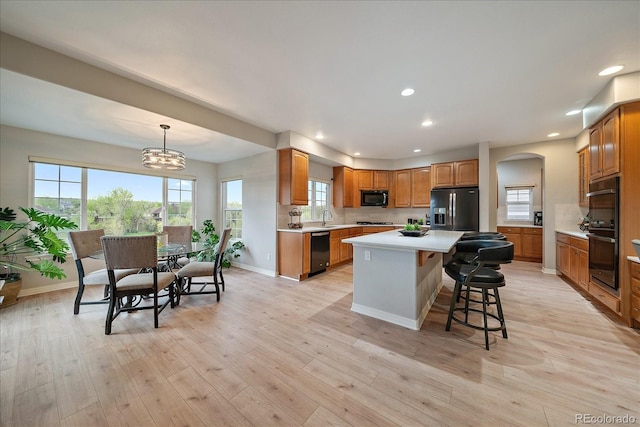 kitchen with black appliances, a sink, light countertops, recessed lighting, and a breakfast bar