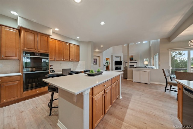 kitchen with dishwasher, tasteful backsplash, light wood-style flooring, light countertops, and a breakfast bar