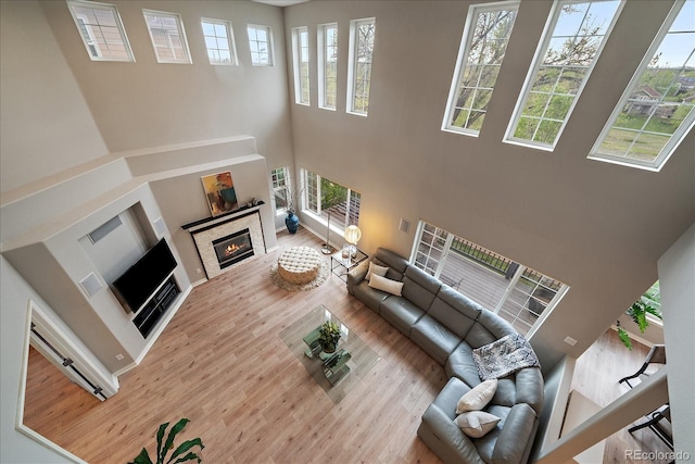 living room featuring a towering ceiling, wood finished floors, and a glass covered fireplace