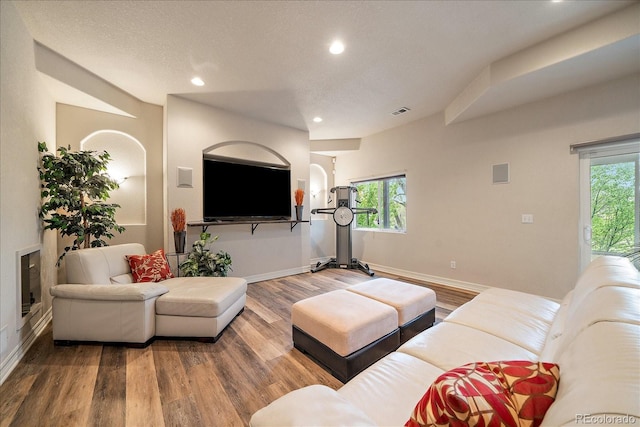 living area with wood finished floors, recessed lighting, baseboards, healthy amount of natural light, and arched walkways