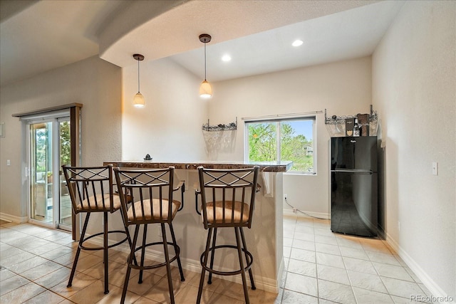 kitchen featuring freestanding refrigerator, plenty of natural light, baseboards, a breakfast bar, and recessed lighting
