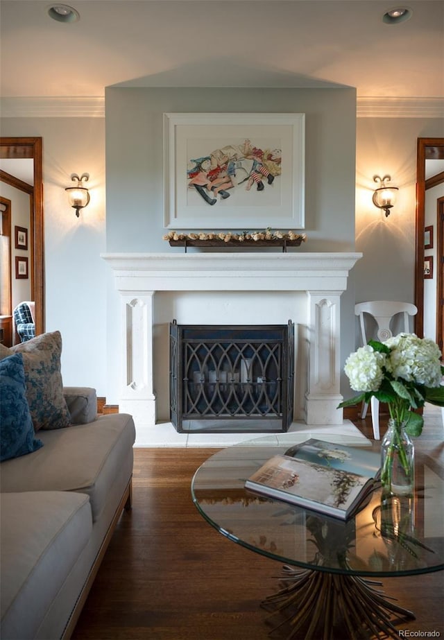 living area with crown molding, wood finished floors, a fireplace with raised hearth, and recessed lighting