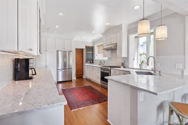 kitchen with a peninsula, appliances with stainless steel finishes, under cabinet range hood, and decorative backsplash