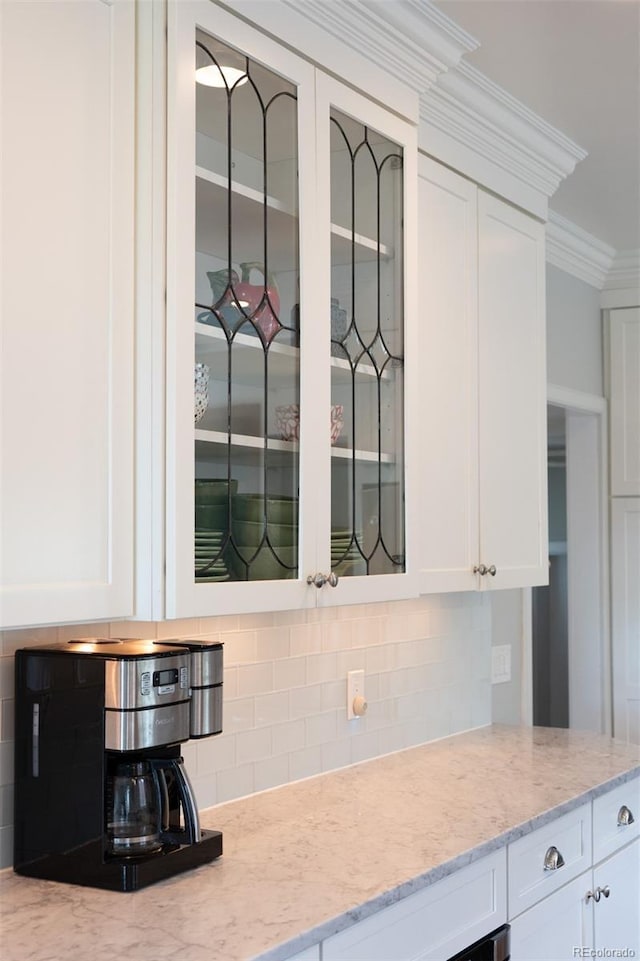 kitchen with glass insert cabinets, white cabinets, decorative backsplash, light stone counters, and ornamental molding