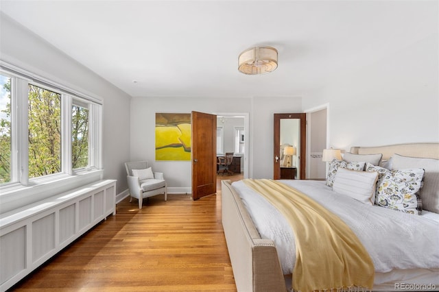 bedroom with baseboards, radiator, and light wood-type flooring