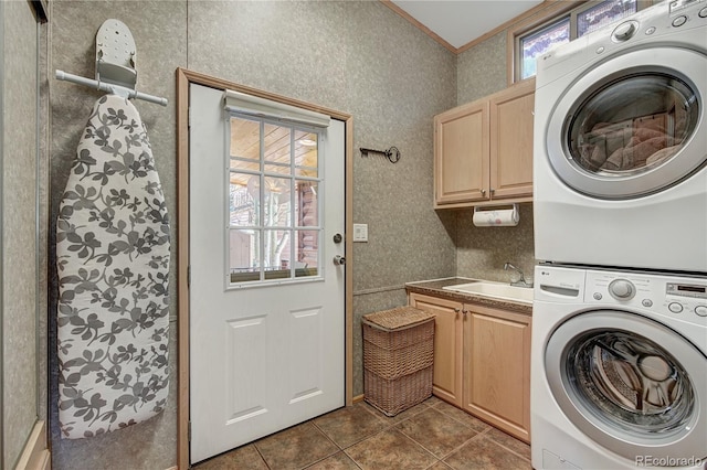 laundry room with cabinets, dark tile patterned floors, crown molding, sink, and stacked washer and dryer