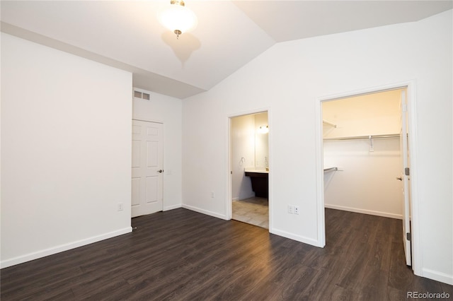 unfurnished bedroom with dark wood-type flooring, ensuite bathroom, vaulted ceiling, a walk in closet, and a closet