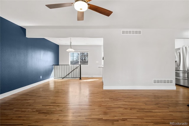 empty room featuring ceiling fan, visible vents, baseboards, and wood finished floors