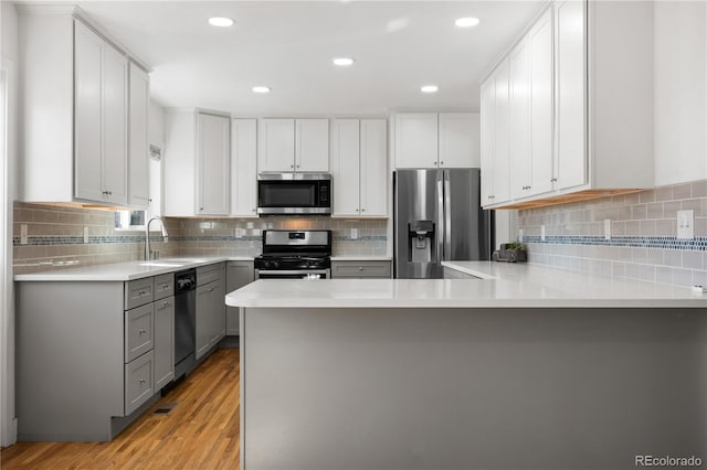 kitchen featuring a peninsula, a sink, gray cabinetry, light countertops, and stainless steel appliances