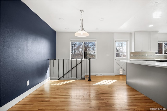 interior space with visible vents, light wood finished floors, light countertops, white cabinetry, and tasteful backsplash