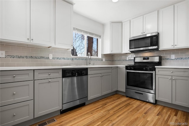 kitchen featuring light wood-type flooring, visible vents, gray cabinets, appliances with stainless steel finishes, and light countertops