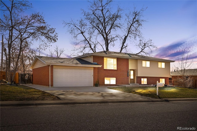 split foyer home with brick siding, fence, concrete driveway, a lawn, and an attached garage