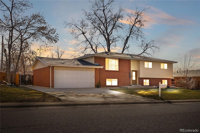 bi-level home with a front lawn, fence, concrete driveway, a garage, and brick siding