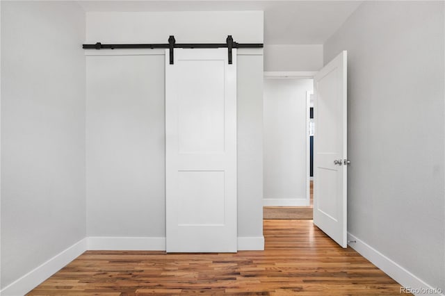 unfurnished bedroom featuring a barn door, baseboards, and wood finished floors