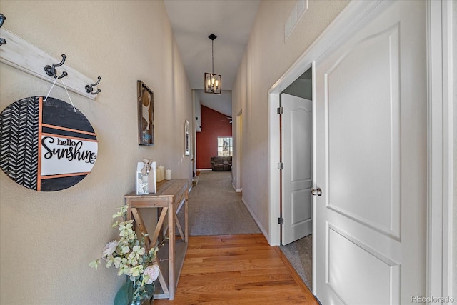 hallway with light wood-style floors, baseboards, visible vents, and a chandelier