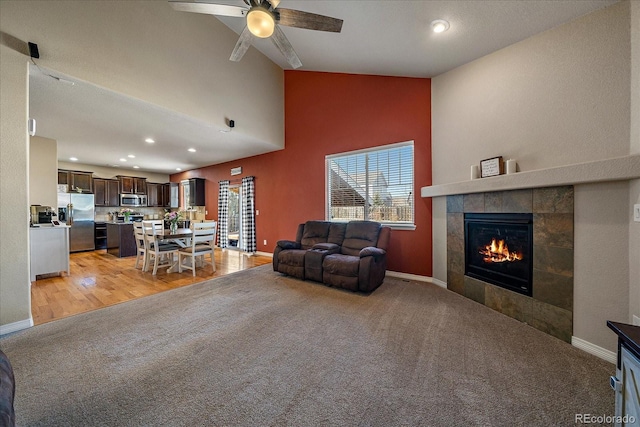 living room featuring light carpet, a fireplace, baseboards, and ceiling fan