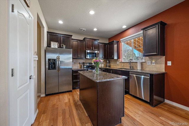 kitchen with light wood-style flooring, dark brown cabinetry, a sink, appliances with stainless steel finishes, and dark stone counters