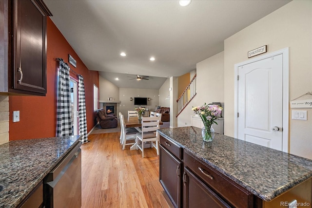 kitchen featuring a warm lit fireplace, dishwasher, ceiling fan, open floor plan, and light wood-type flooring