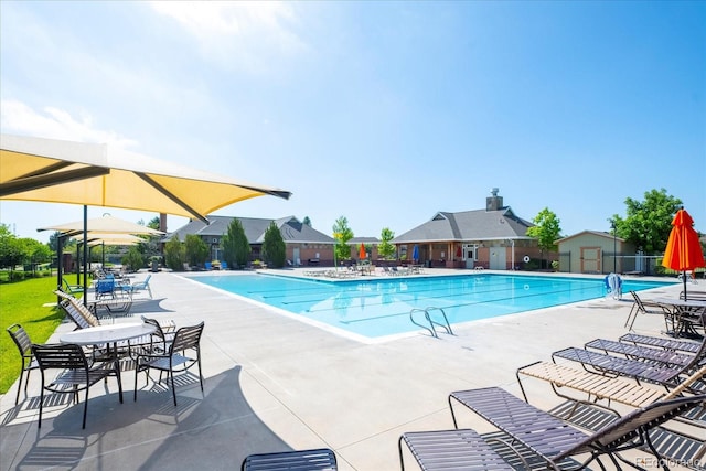 community pool with an outbuilding, a patio area, and fence