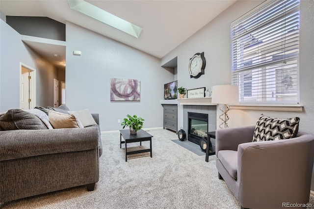 carpeted living room featuring vaulted ceiling with skylight and a tiled fireplace