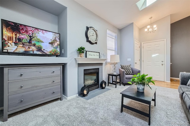 living room with a notable chandelier, a tiled fireplace, lofted ceiling with skylight, and light hardwood / wood-style flooring