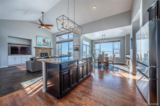 kitchen featuring hanging light fixtures, stainless steel fridge, dark stone counters, a fireplace, and a kitchen island