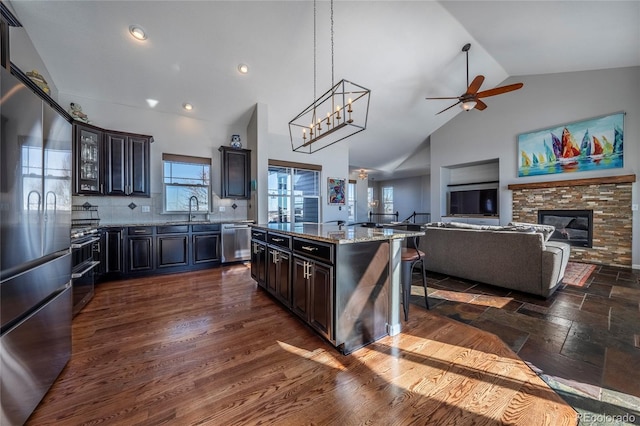 kitchen featuring appliances with stainless steel finishes, backsplash, sink, a center island, and a stone fireplace