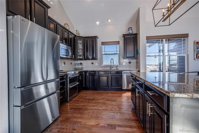 kitchen featuring sink, vaulted ceiling, dark stone countertops, appliances with stainless steel finishes, and tasteful backsplash