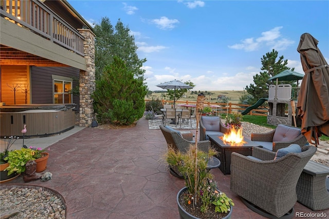 view of patio / terrace with a playground, a balcony, a hot tub, and an outdoor fire pit