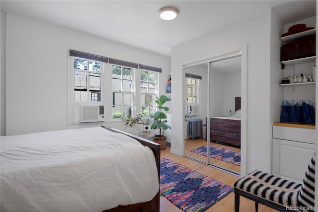 bedroom featuring radiator heating unit, light wood-type flooring, cooling unit, and a closet