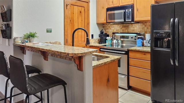 kitchen featuring light tile patterned flooring, appliances with stainless steel finishes, a kitchen bar, decorative backsplash, and light stone countertops