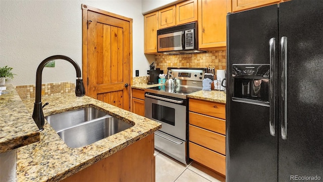 kitchen featuring sink, tasteful backsplash, light stone counters, light tile patterned floors, and stainless steel appliances